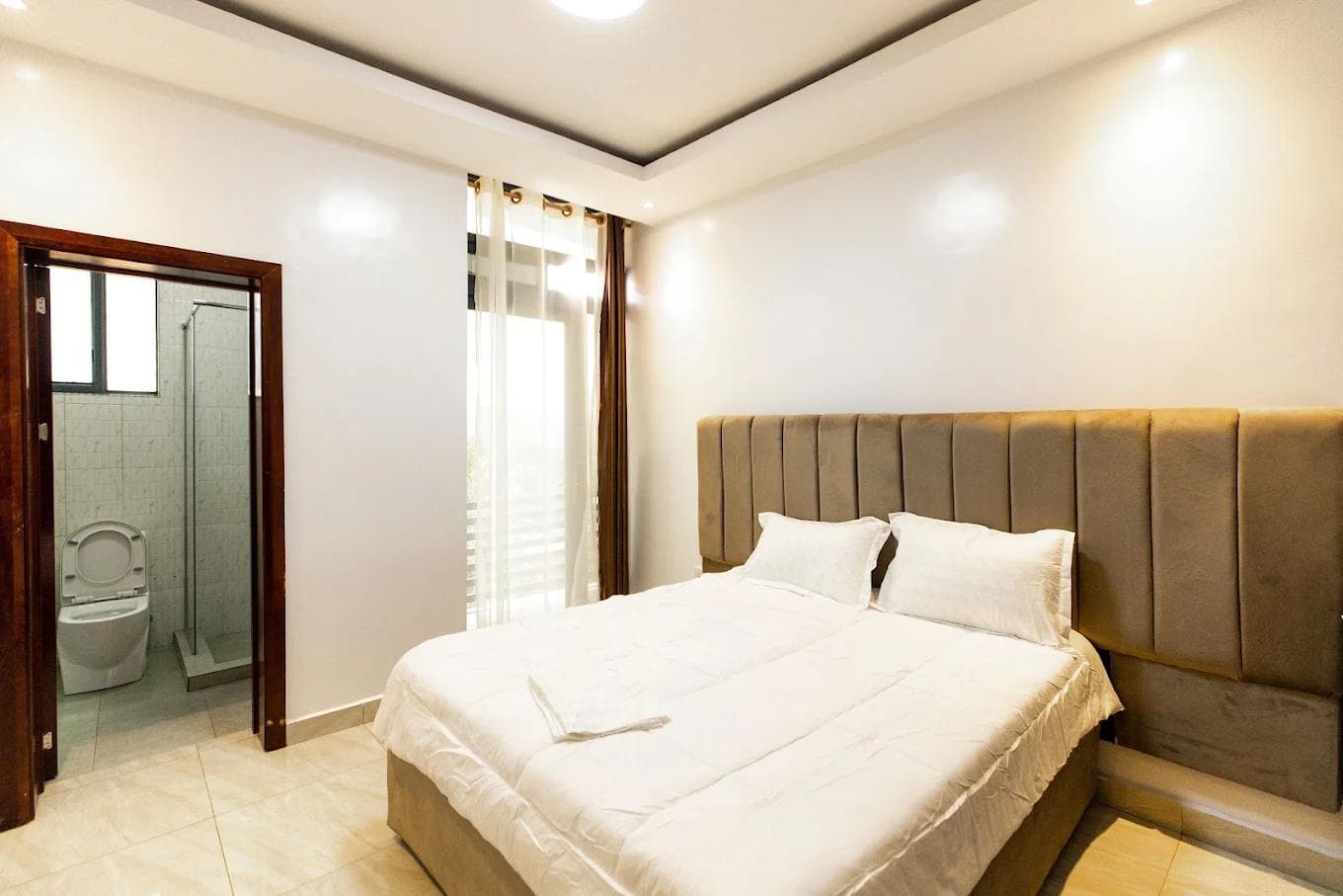 Second bedroom at Laurus Apartments, Kigali, with a double bed, upholstered headboard and en-suite shower room