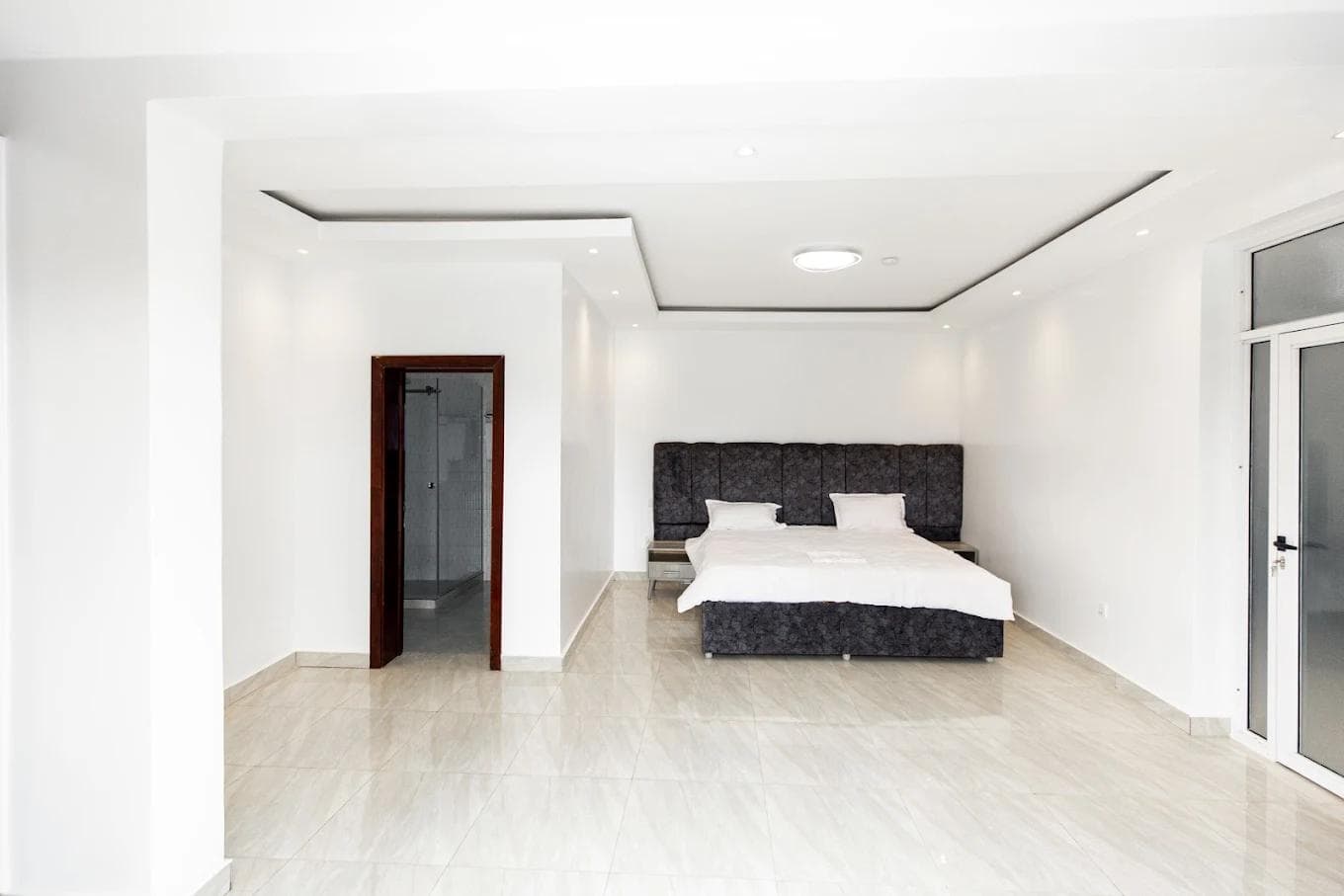 Master bedroom at Laurus Apartments, Kigali, with a double bed, en-suite doorway and balcony doors